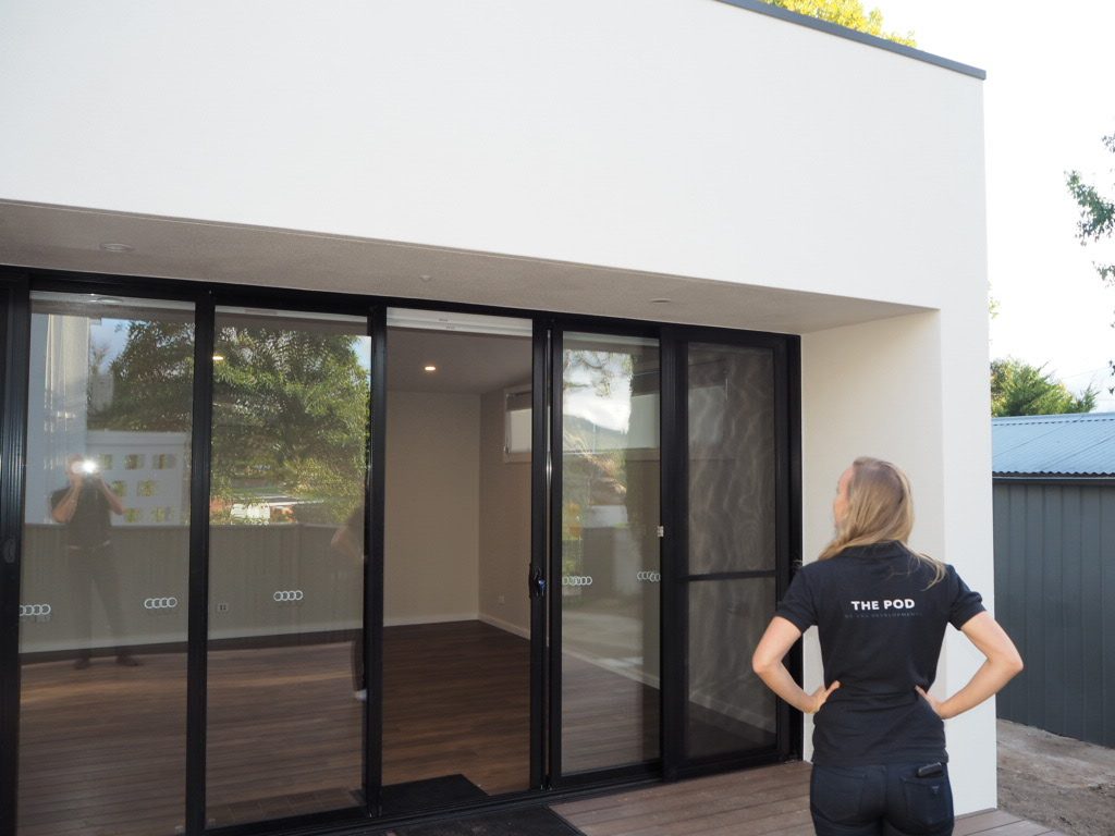 Jacqueline Valk, in a black The Pod work shirt, standing in front of a completed secondary dwelling build
