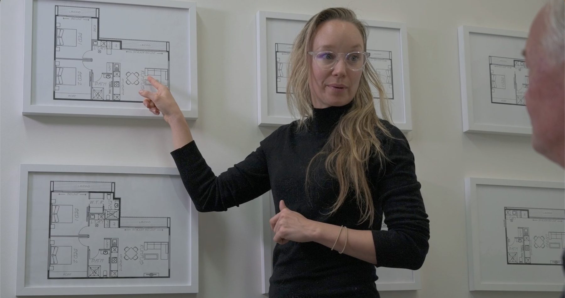 Jacqueline pointing to a framed floor plan while explaining a design